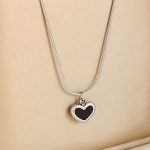 Macro shot of silver necklace featuring a black heart-shaped pendant on textured background