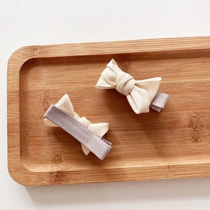 Sweet cream and grey bow hair clips for girls on a textured wooden tray background