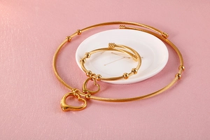 Flat lay of gold heart pendant wire necklace and matching bracelet set on pink leather