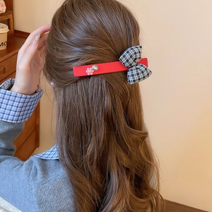Detail of red hair clip with black and white plaid bow and pink flower worn by a model