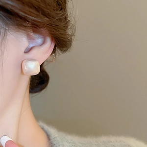 Macro view of gold-plated square sugar cube pearl stud earrings worn by a model