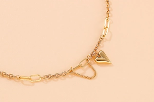 Détail du collier à pendentif coeur doré avec maille mixte sur une surface beige doux