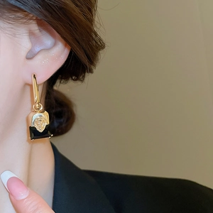 Detailed close-up of a gold-plated lion head earring featuring a black rectangular stone