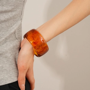 Detailed close-up of retro amber resin bangle with marbled textures on a model wrist