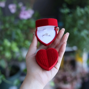Macro shot of an open red heart jewelry box with a ring inside held in a garden setting