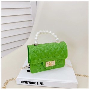 Detail of green mini jelly bag with pearl handle and golden chain on a book background