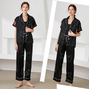 Detail of black silk pajamas featuring white line art face print and contrast piping
