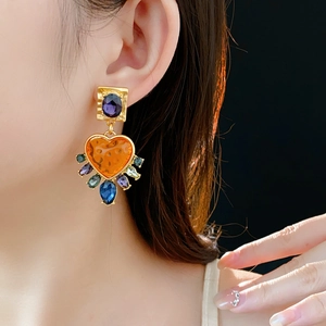 Detail showing vintage gold earrings with orange heart stone and colorful gems on model