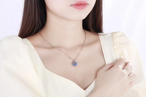 Detail of rose gold coin necklace with blue enamel pendant worn on a model's neck