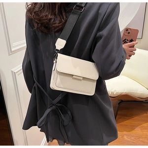 Detail of a creamy white flap square bag with a wide black woven shoulder strap on a model