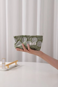 Close-up of dark green canvas makeup bag with white floral embroidery and zipper closure