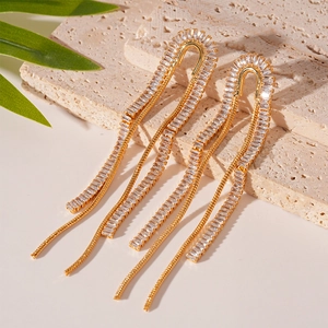 Close-up of elegant gold tassel earrings with white zircon on a stone surface
