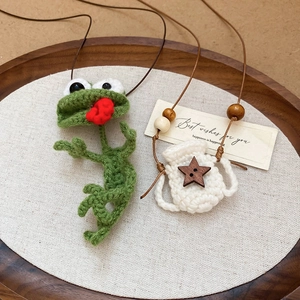 Detail of hand-crocheted green frog and white bag pendant with wooden star button on tray