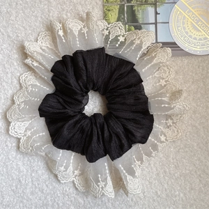 Detail of elegant black fabric scrunchie with white lace embroidery and floral texture