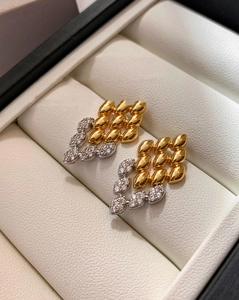 Macro d'oreilles géométriques en or et argent présentées dans une boîte à bijoux blanche