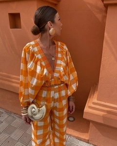 Detail of V-neck puff sleeve crop top and wide-leg trousers in orange plaid pattern