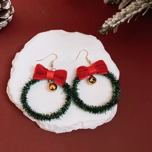 Close-up of green wire Christmas wreath earrings with red velvet bow and golden bell