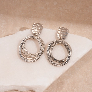 Détail de boucles d'oreilles géométriques argentées martelées sur une pierre
