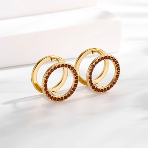 Macro shot of gold circular earrings with red zircon inlays on white stairs background
