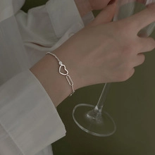 Detail of silver geometric layered chain bracelet with heart pendant on woman's wrist