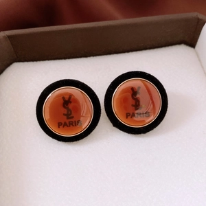 Close-up of vintage round earrings with black flocking and amber logo inlay on white cushion
