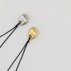 Detailed view of teardrop bean pendants in polished gold and silver on black cords