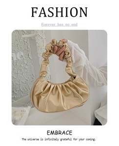 Detail of champagne gold ruched cloud bag showing smooth faux leather texture and handle