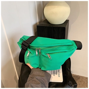 Close-up of bright green multi-pocket crossbody bag with adjustable black strap on a stand