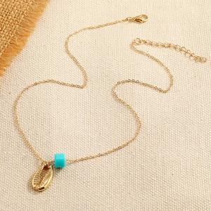 Minimalist gold necklace featuring turquoise beads and sea shell pendant on woven cloth