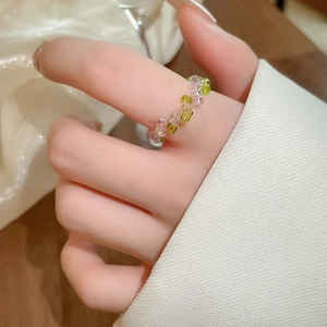 Close-up of pink and green beaded elastic flower ring worn on a finger in soft lighting