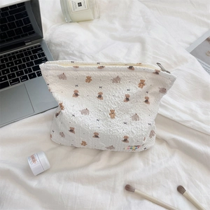 Detailed view of white cartoon bear makeup bag with 'sozak' tag on cozy white sheets