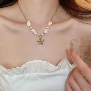 Detail of starfish and pearl pendant necklace worn by model on neck with seashell accents