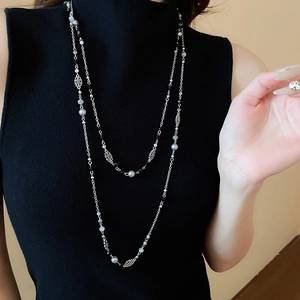Detail of layered silver necklace with grey pearls and flower charms on a black sweater