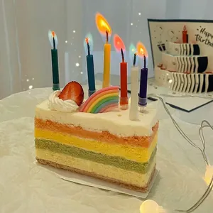 Rainbow gradient candles lit on top of a colorful layered cake in a cozy atmosphere