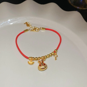 Détail d'un bracelet tressé rouge avec pendentifs sac de chance dorés et lingots d'or