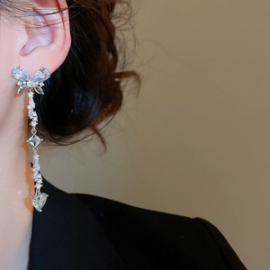 Detail of butterfly heart tassel earring with blue zircons worn by a model
