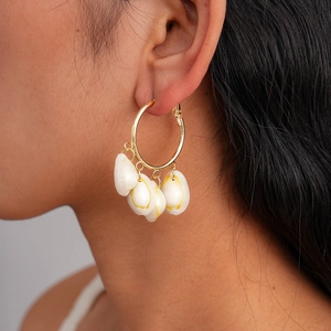 Close-up of gold hoop earrings with hanging natural white cowrie shell pendants on model
