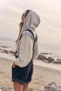 Close-up of grey hoodie with cream chunky cable knit sleeves and denim dungarees