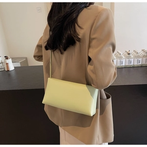 Shoulder view of a mint green matte leather baguette bag worn with a brown blazer