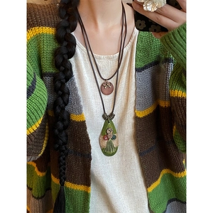Detailed view of Bohemian bow and green teardrop tassel necklace on knit sweater