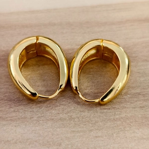 Detailed view of teardrop gold hoop earrings on a light wood background texture