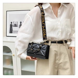 Detail of black quilted crossbody bag with chunky chain and jacquard wide strap on model