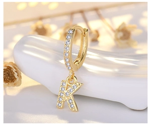 Macro detail of gold letter K earring with sparkling zircons and a secure hoop closure