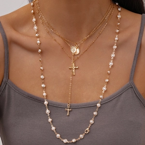 Close-up of layered gold necklaces with pearl accents, cross pendant, and relief coin charm