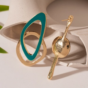 Gros plan de boucles d'oreilles dorées asymétriques avec émail sarcelle sur céramique