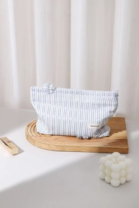Dettaglio della borsa trucco a righe con nodo decorativo su supporto di legno