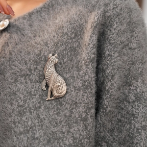 Detailaufnahme einer Vintage-Katzenbrosche aus Metall auf einem grauen Strickpullover