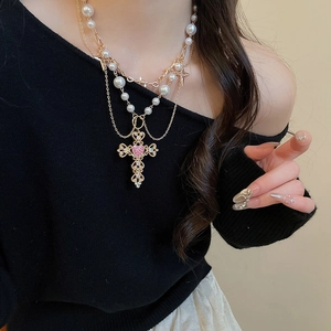 Close-up of layered necklace with pearl chain and cross pendant featuring a pink heart gem