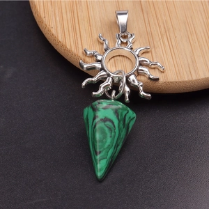 Detalle del colgante de sol plateado con una piedra de malaquita verde sobre madera