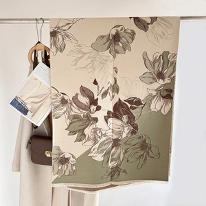 Detail of beige and green cashmere scarf with floral pattern and fringe hanging on a rack